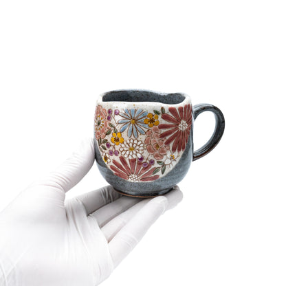 Red floral Kutani mug held in a gloved hand to show scale.