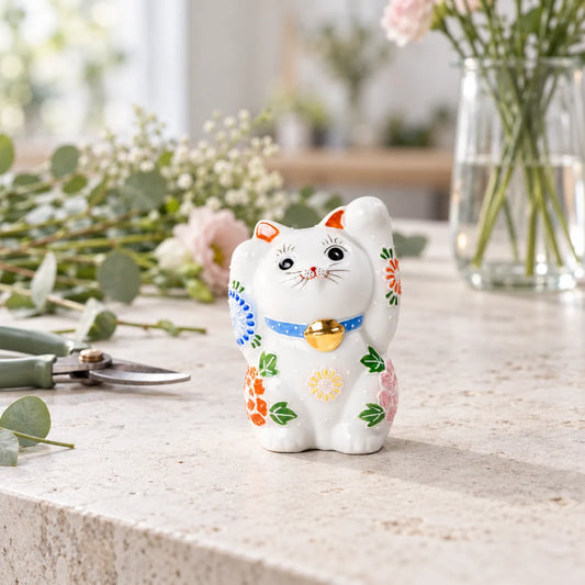 White Hanazono lucky cat with raised floral details on a florist worktable beside cut stems and pruning snips