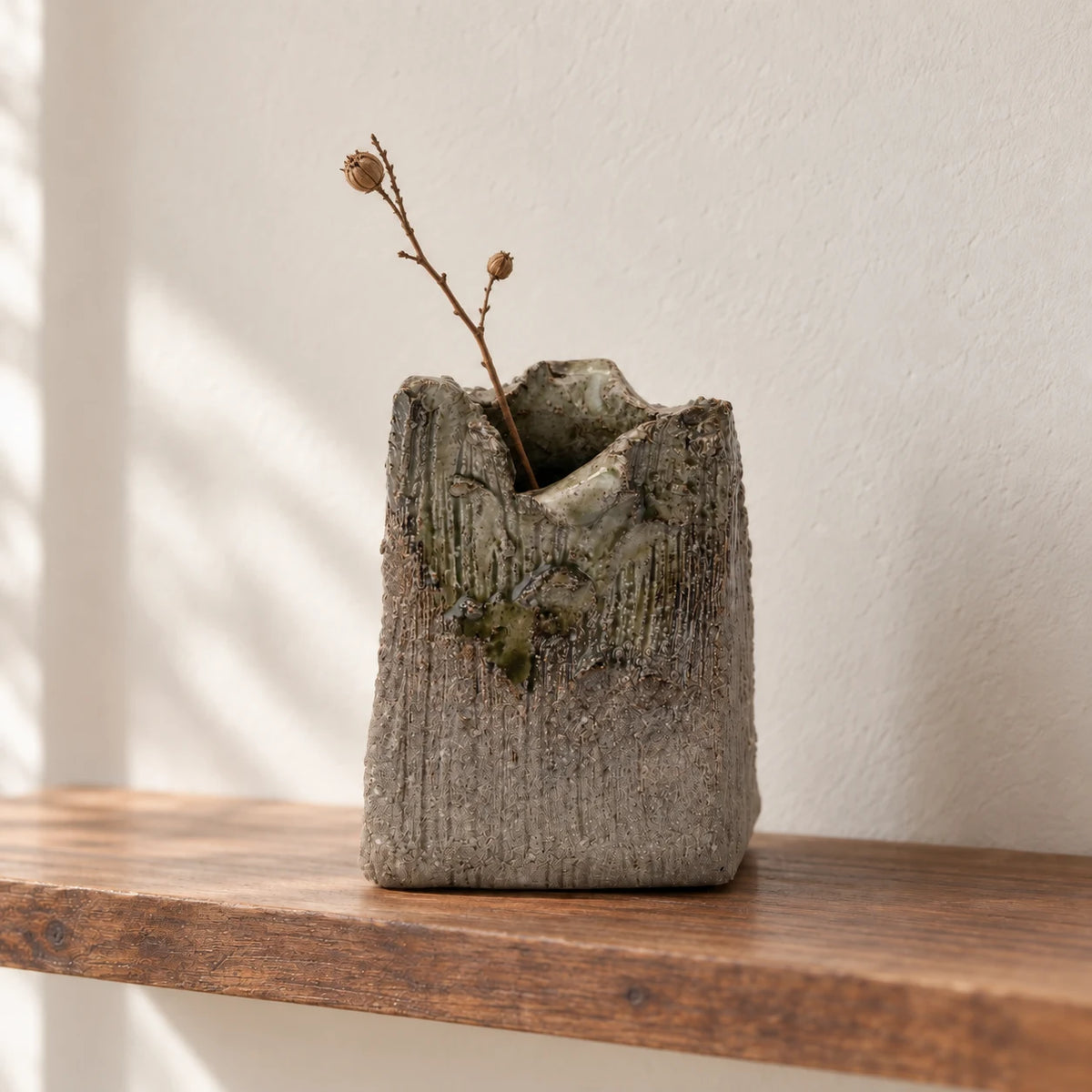 Gray Shigaraki rectangular bud vase holding a slender dried branch with seed pods on a wood shelf.