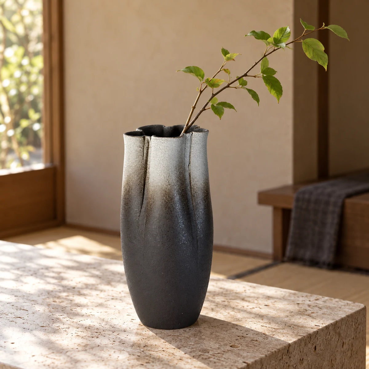 Tall black and white Hechimon Zansetsu vase with a single leafy branch on a pale stone table.