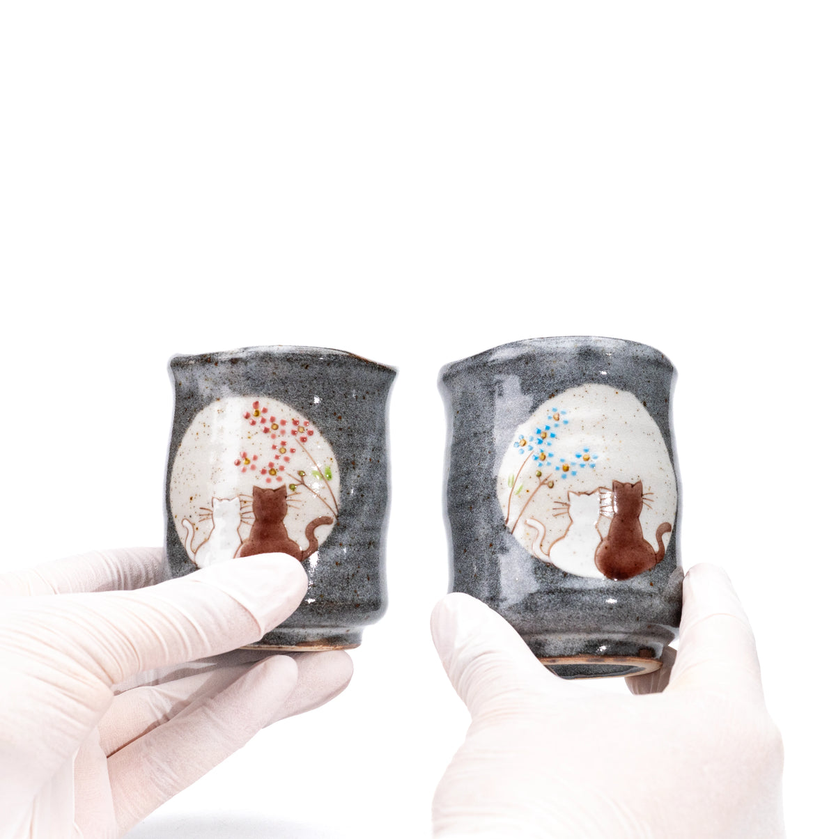 Kutani cat yunomi pair held in gloved hands to show their different sizes.