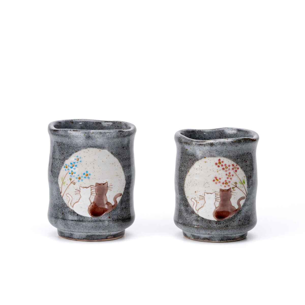 Larger and smaller gray Kutani yunomi cups with cats beneath blue and pink flowering trees.