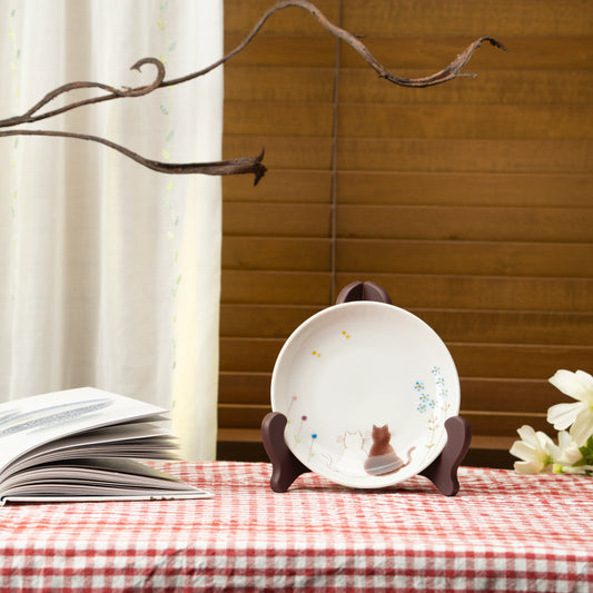 Cat plate displayed on a stand on a red checked tablecloth beside a book.