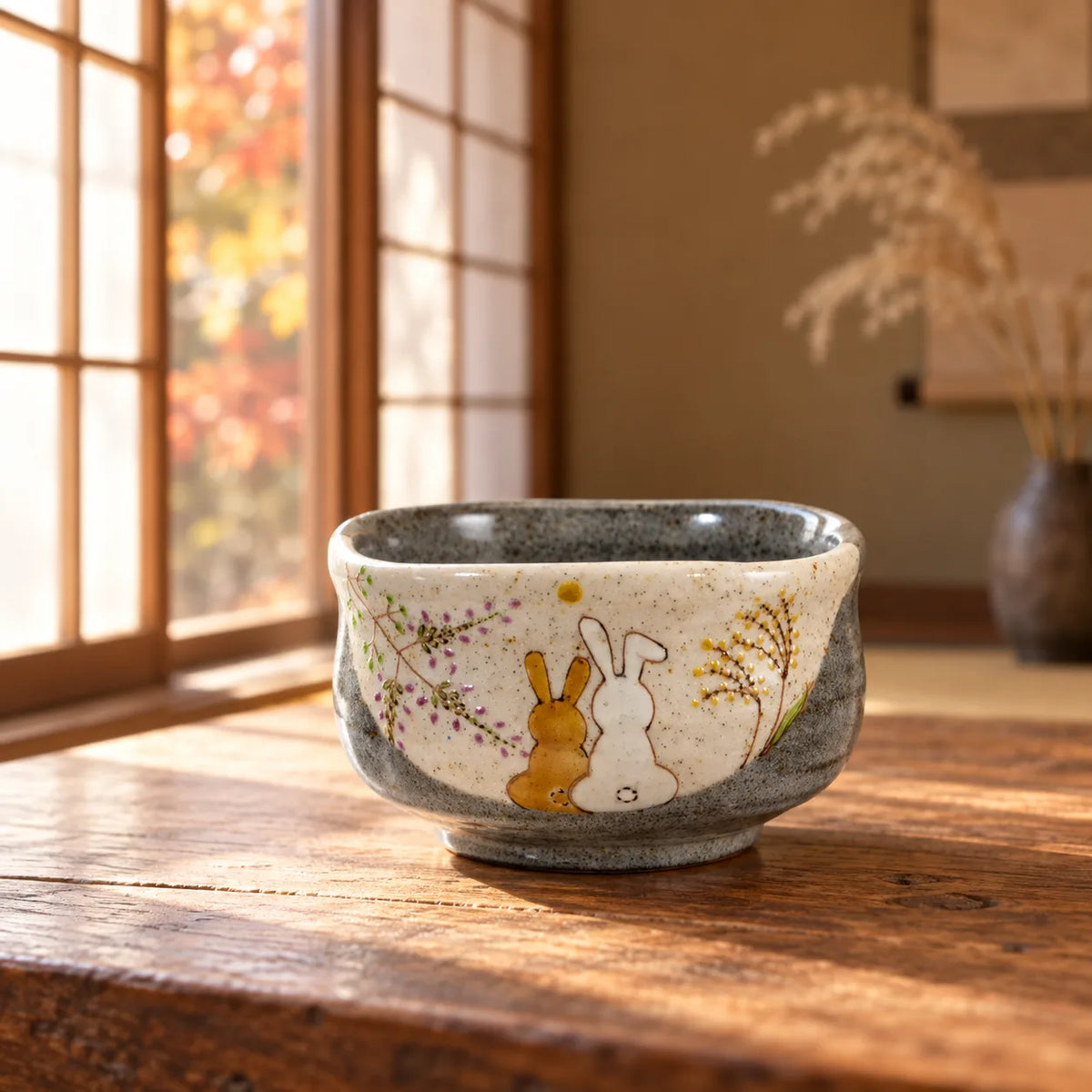 Iroe Yu Hidamari rabbits matcha bowl on a sunlit wooden table, showing the painted moon and autumn grasses.
