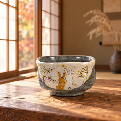 Iroe Yu Hidamari rabbits matcha bowl on a sunlit wooden table, showing the painted moon and autumn grasses.