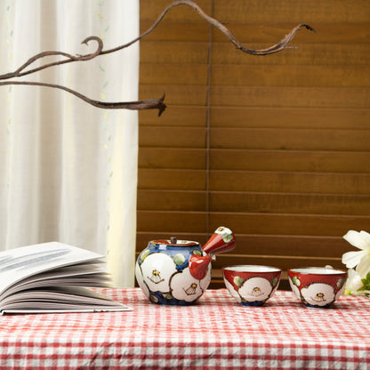 Camellia teapot and two cups on a red checked tablecloth beside a book and flowers.