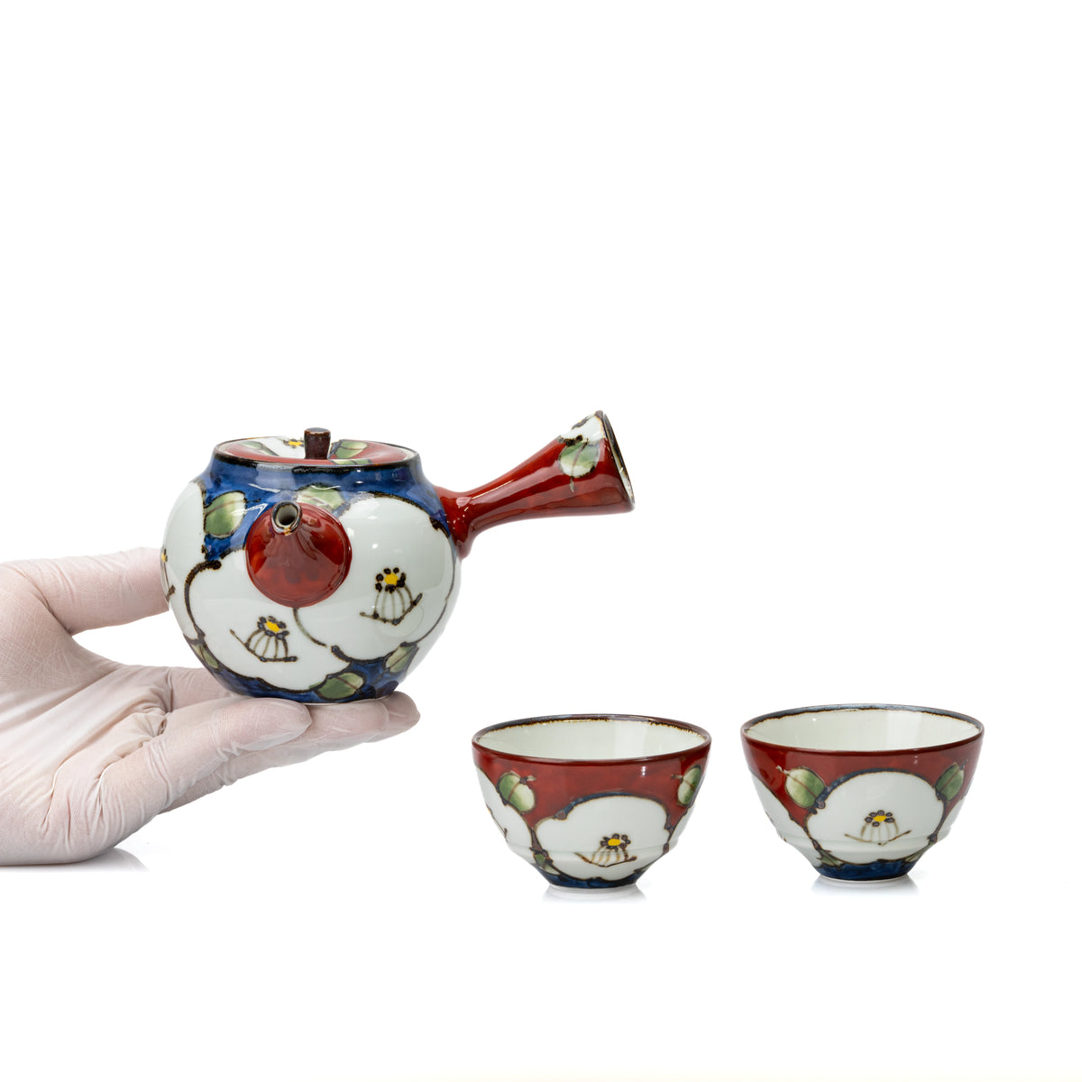 Camellia teapot held in a gloved hand beside its two cups.