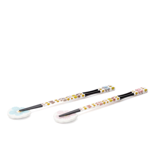 Two pairs of black chopsticks with floral handles and blue and pink porcelain rests on white.