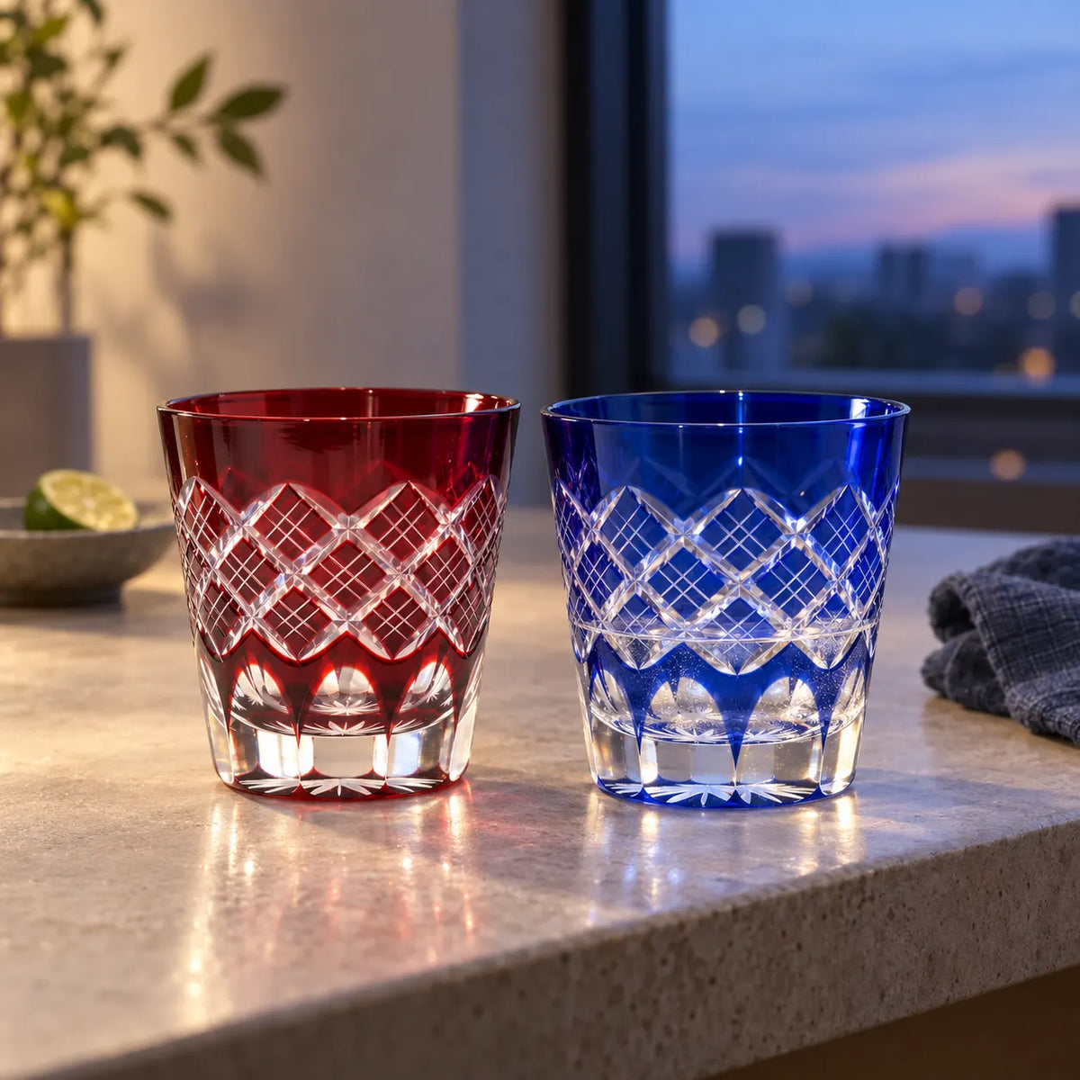 Red and blue Kasane Yarai Edo Kiriko tumblers with layered lattice cuts on a stone counter at dusk
