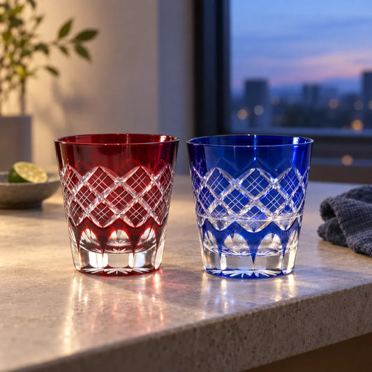 Red and blue Kasane Yarai Edo Kiriko tumblers with layered lattice cuts on a stone counter at dusk