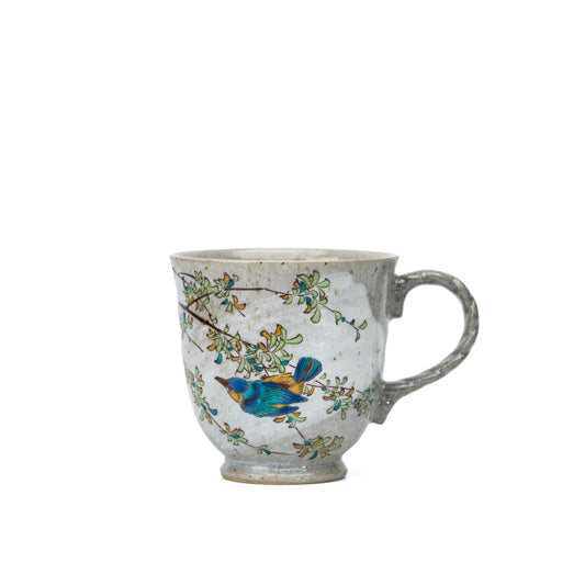 Front view of a Kutani kingfisher mug with a blue kingfisher and leafy branches on a white background.