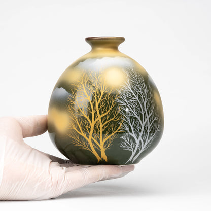 Tree-patterned Kutani bud vase held in a gloved hand.