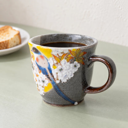 Kutani Yoshidaya bird-and-cherry mug filled with coffee on a pale green breakfast table, with toast in the background.