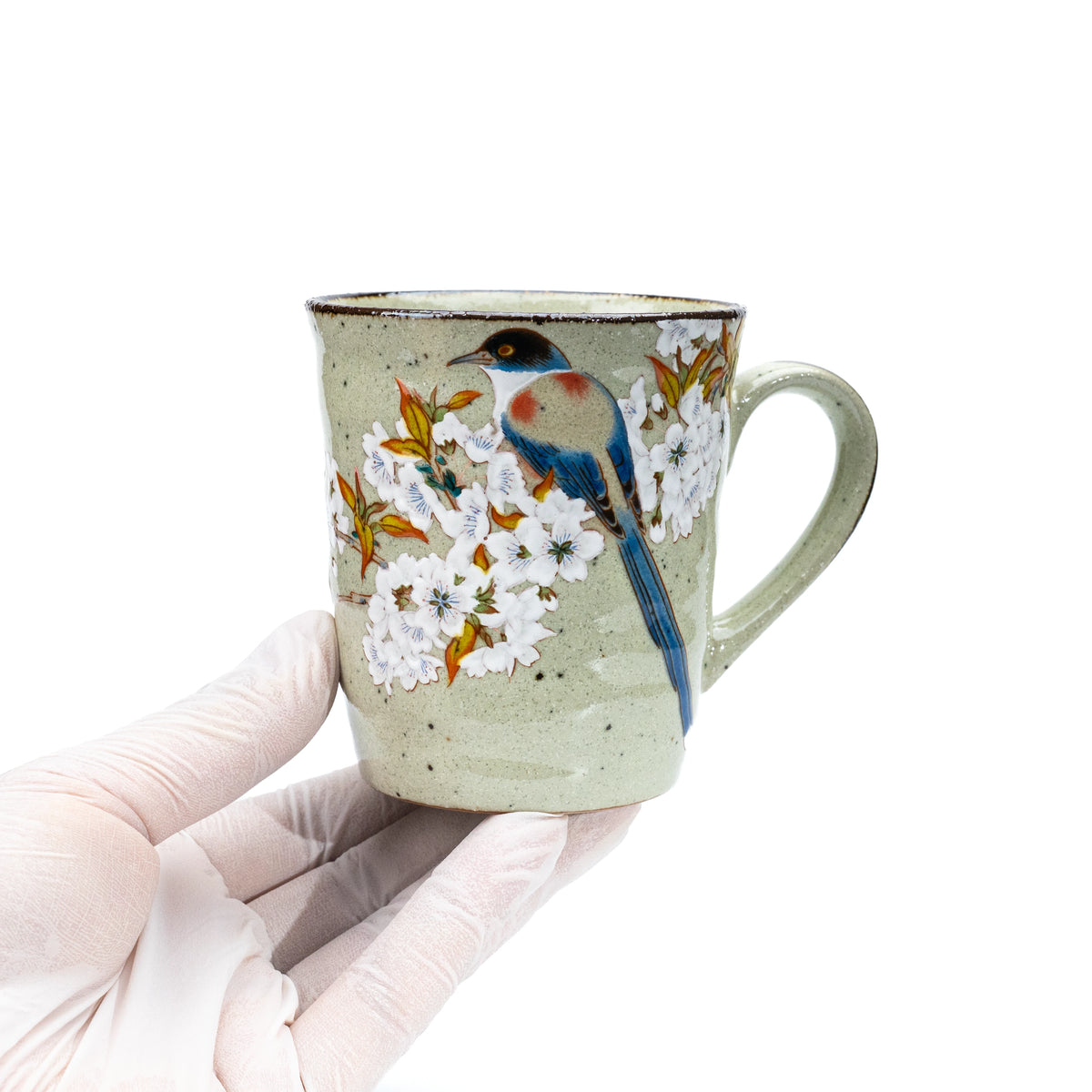 Kutani cherry blossom and bird mug held in a gloved hand.