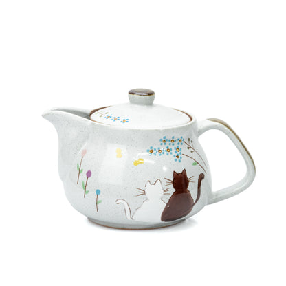 Pale gray Kutani teapot with two seated cats, small flowers and a rounded handle on white.