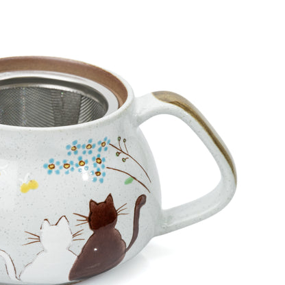 Close-up of two cats, painted flowers and the brown teapot handle.