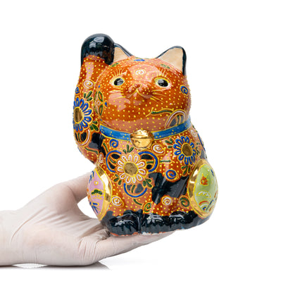 Large orange and black floral lucky cat held in gloved hands.