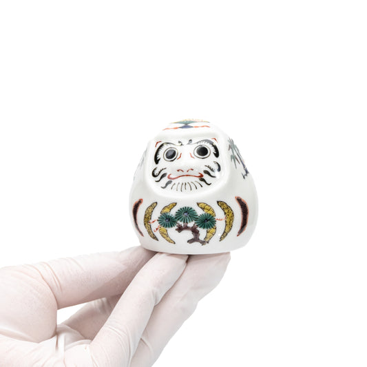 Small white Kutani daruma held in a gloved hand.