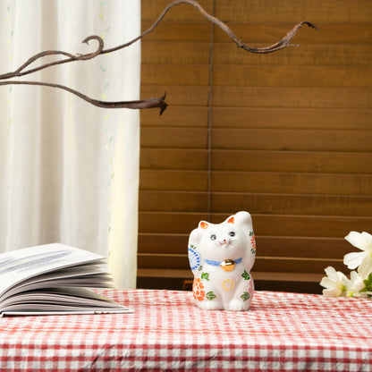 White floral lucky cat on a red checked tablecloth beside a book.