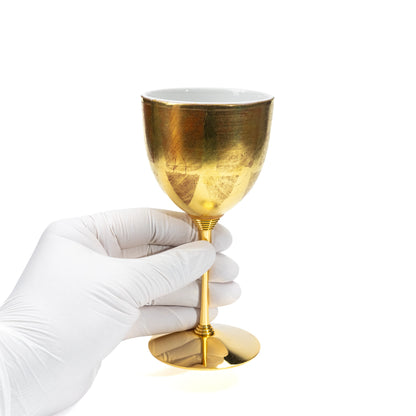 Gold-stemmed wine cup held in a gloved hand.