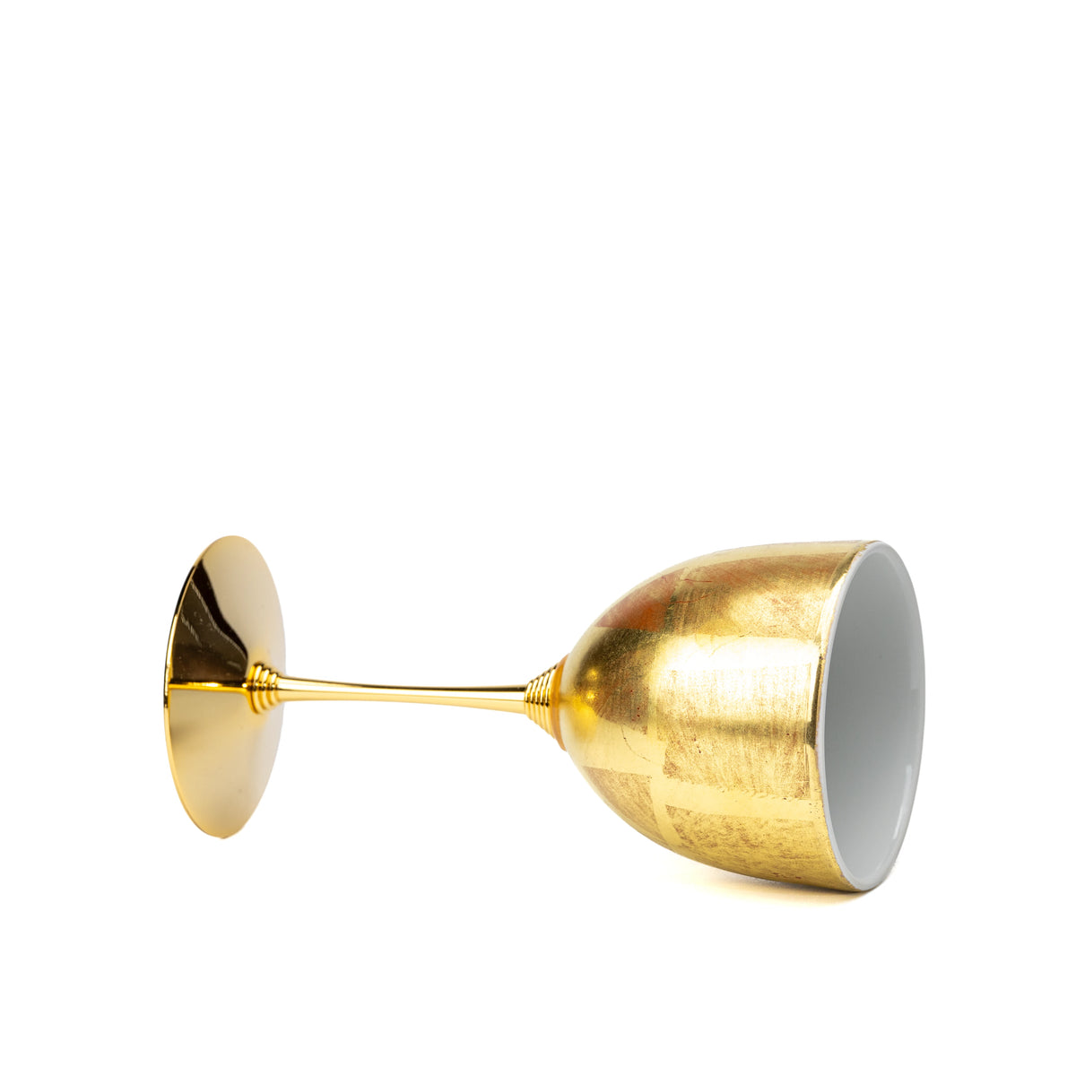 Side view of the gold wine cup lying on white.