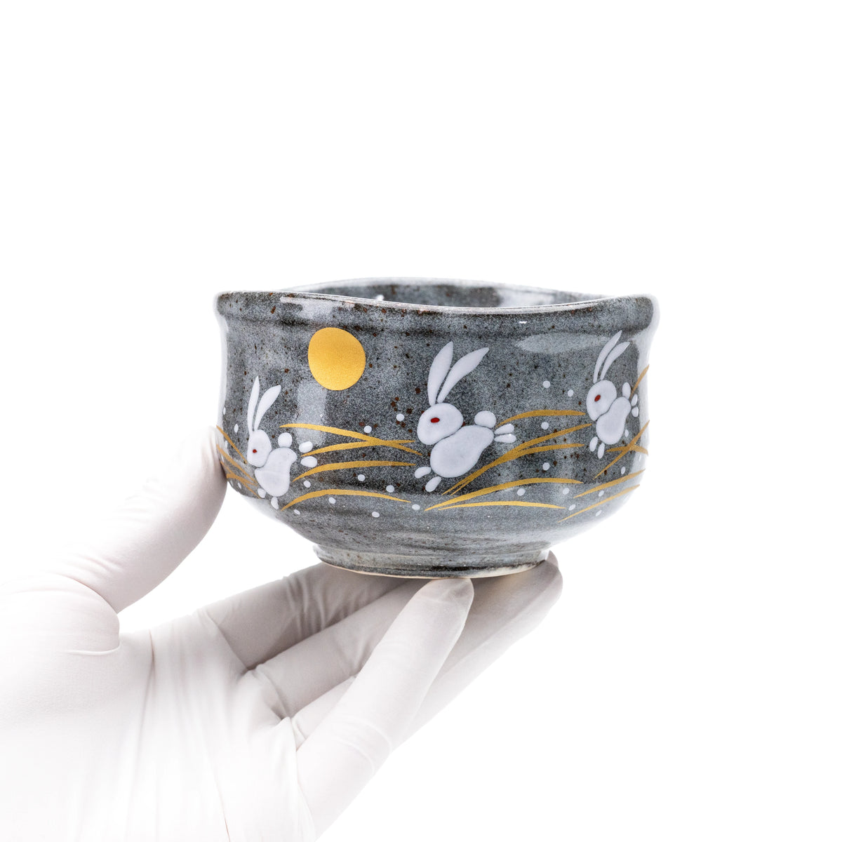 Leaping rabbits matcha bowl held in a gloved hand.