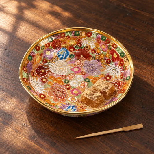 A shallow Kutani Kinhanazume serving bowl holding two small kinako-dusted warabi mochi, with its floral pattern visible