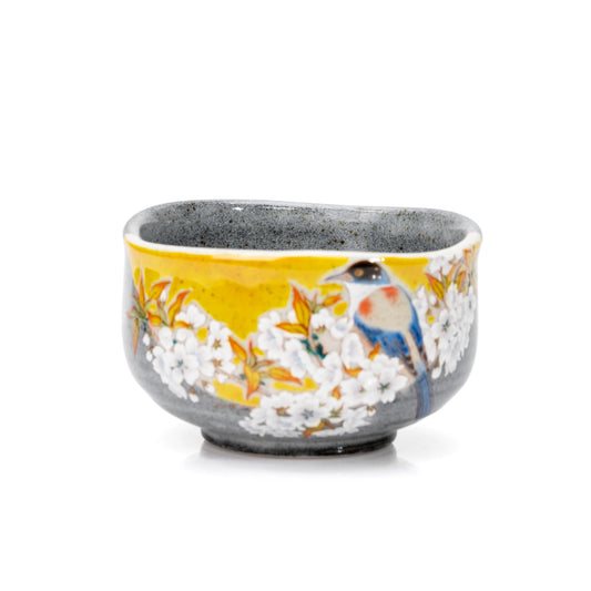 Gray Kutani matcha bowl with a blue bird and white cherry blossoms on a yellow panel.