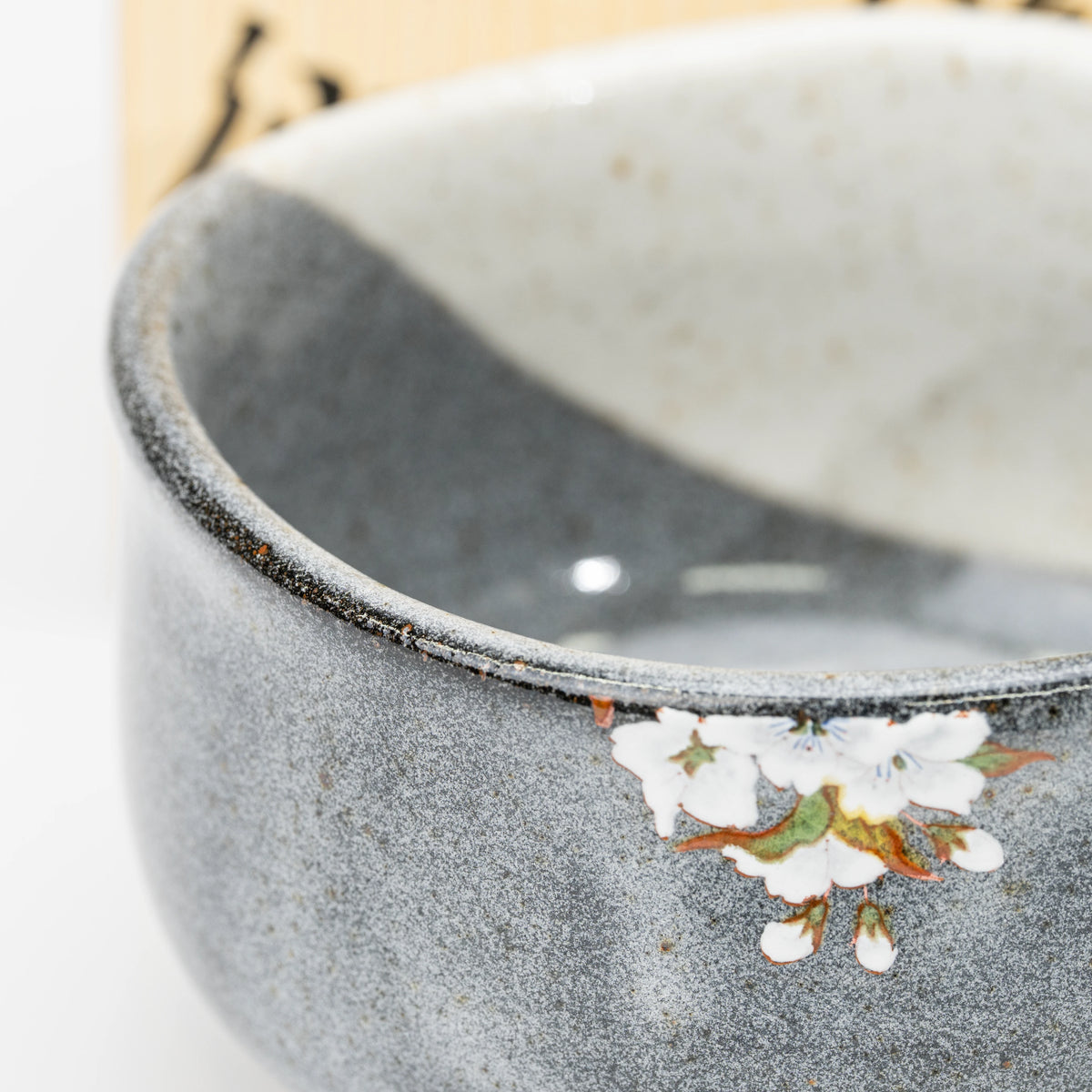 Close-up of gray glaze and small white blossoms near the rim.
