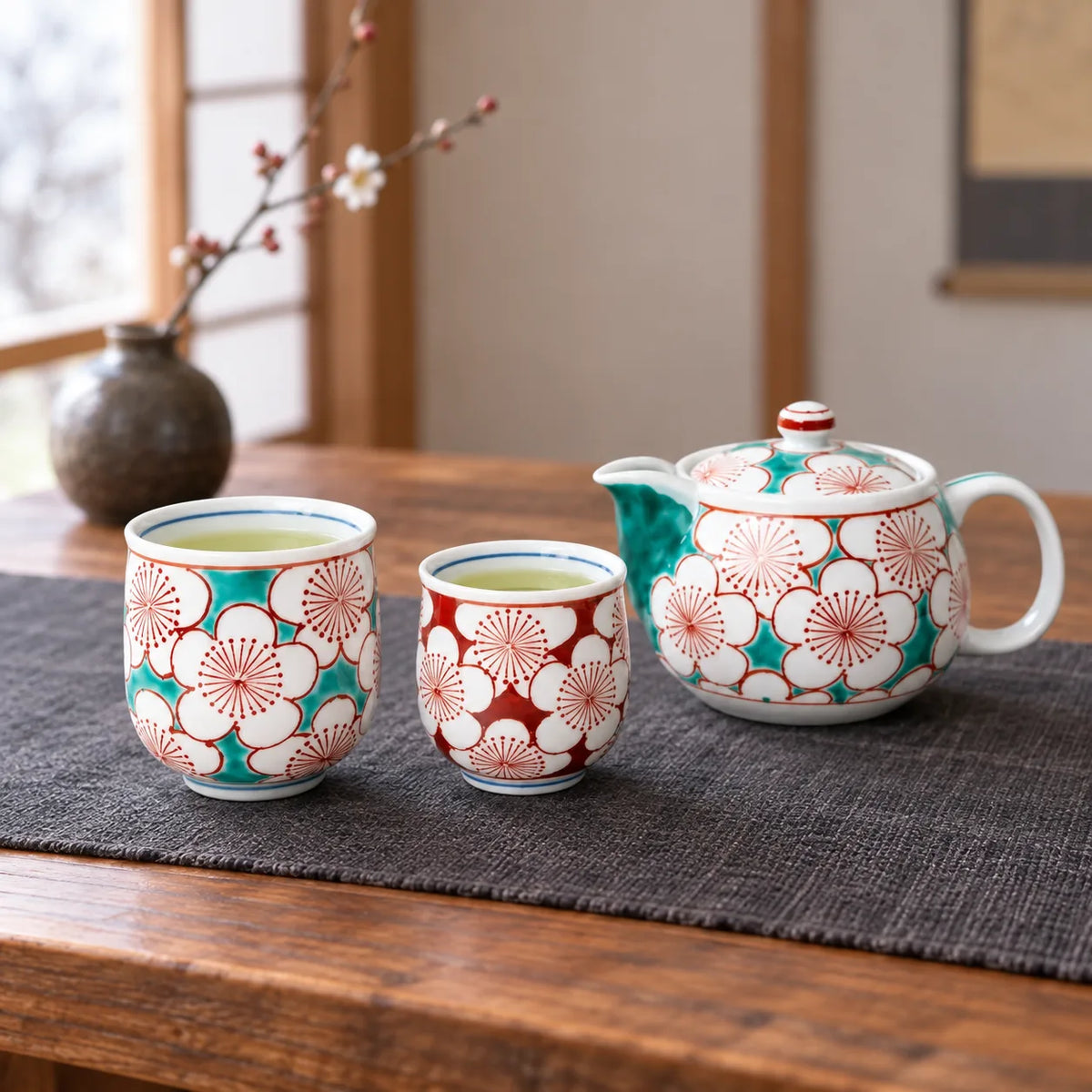 Kutani plum blossom teapot with a larger turquoise cup and smaller red cup on a low table