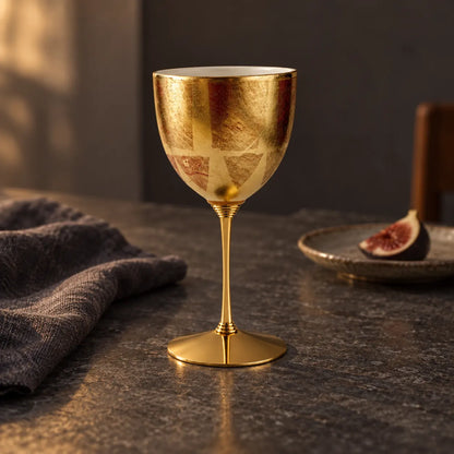Single red and gold Kutani porcelain wine cup on a brass stem beside a fig on a dark table