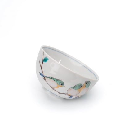 White Kutani rice bowl with painted green and yellow birds, tilted on white.
