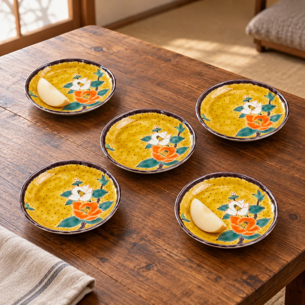 Five yellow Kutani camellia plates on a wooden table, two holding small pear slices while the floral patterns remain visible