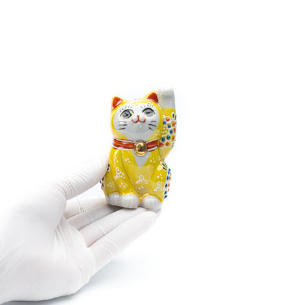 Small yellow lucky cat held in a gloved hand.