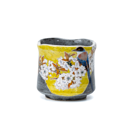 Yellow and gray Kutani yunomi with a blue bird among white cherry blossoms on white.