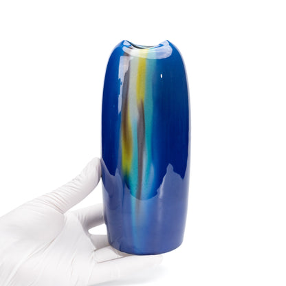 Tall blue glazed vase held in a gloved hand.