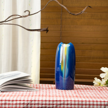Blue glazed porcelain vase on a red checked tablecloth beside a book.