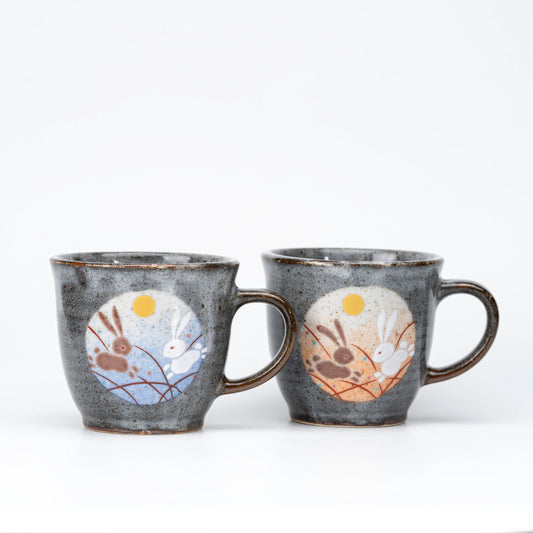 Gray Kutani mug pair with leaping rabbits beneath golden-colored moons on blue and orange panels.