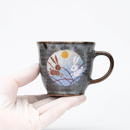 Blue-panel rabbit mug held in a gloved hand.