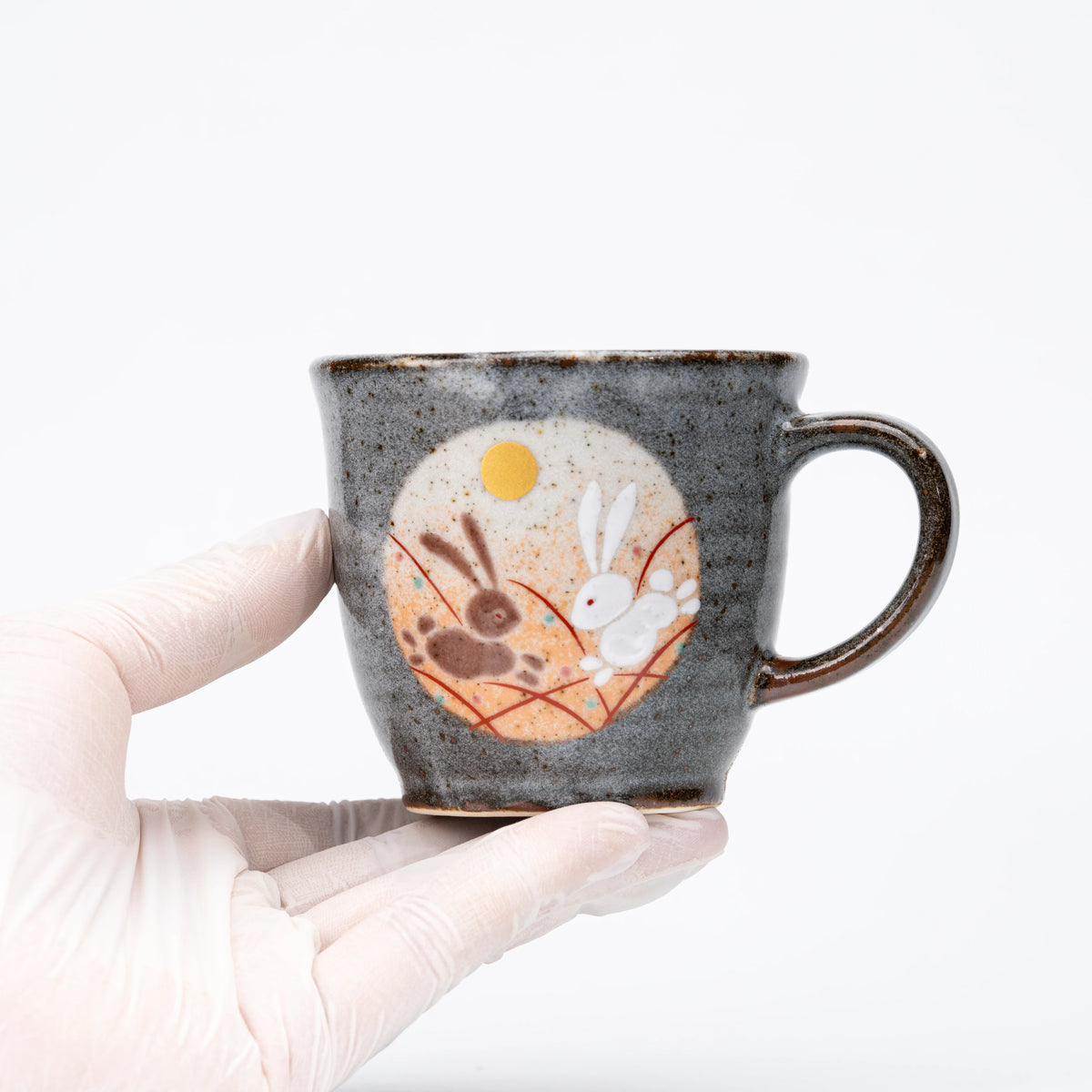 Orange-panel rabbit mug held in a gloved hand.