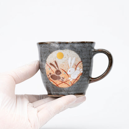 Orange-panel rabbit mug held in a gloved hand.