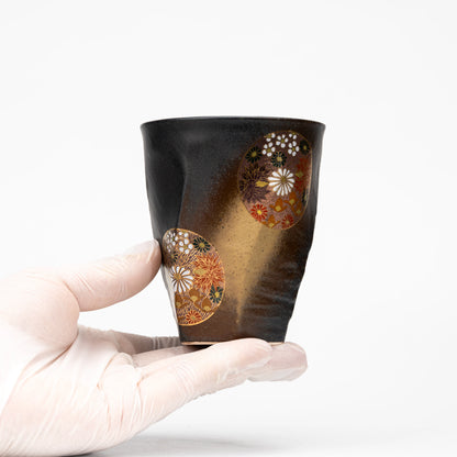 Black floral Kutani cup held in a gloved hand to show scale.