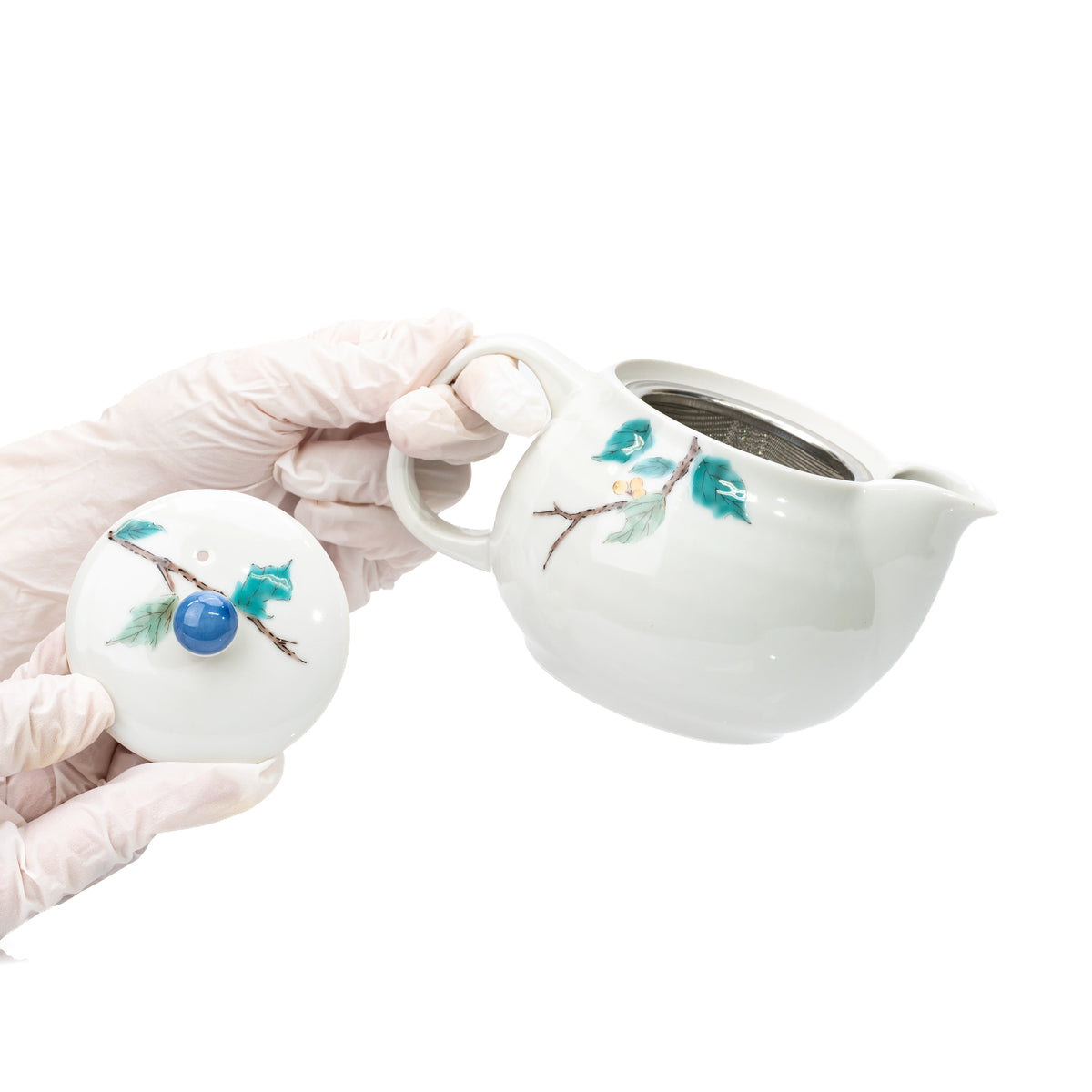 Gloved hands lifting the lid to reveal the mesh strainer inside the Kutani teapot.