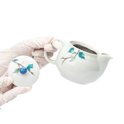 Gloved hands lifting the lid to reveal the mesh strainer inside the Kutani teapot.