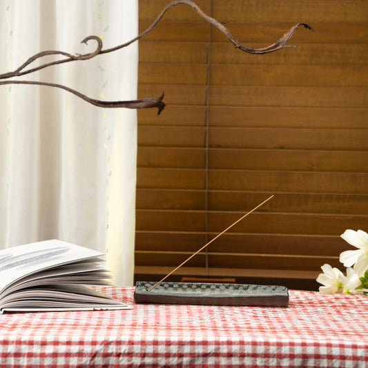 Green mosaic incense holder on a red checked tablecloth beside a book and white flowers.