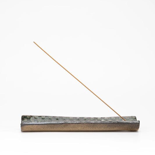 Long Hechimon incense holder with green mosaic glaze and an incense stick on a white background.