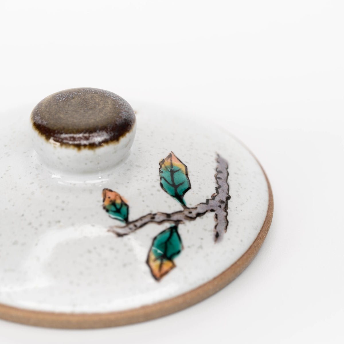 Close-up of the Kutani owl teapot lid with a brown knob and painted leaves.