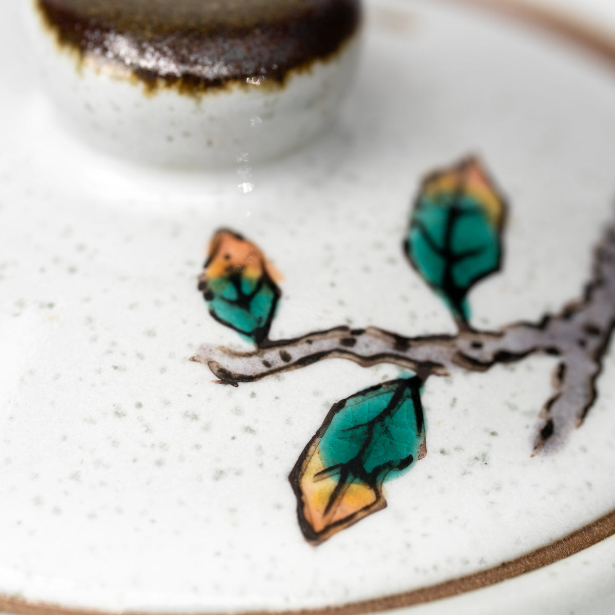 Close-up of a leafy branch beside the Kutani teapot lid knob.