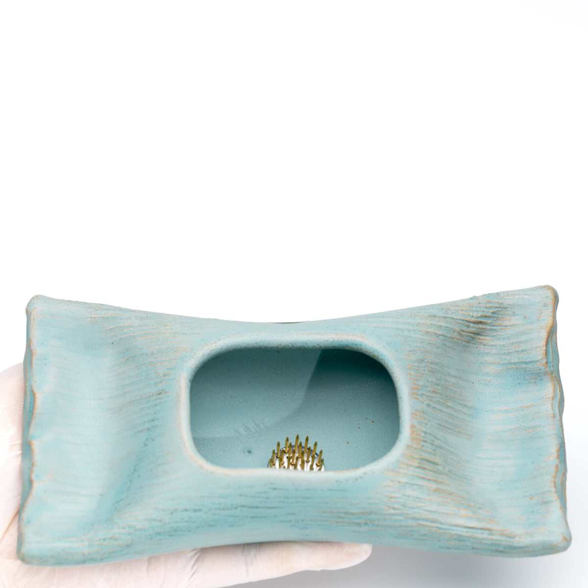 Pale blue vase held in a gloved hand, with a small flower pin holder visible inside.