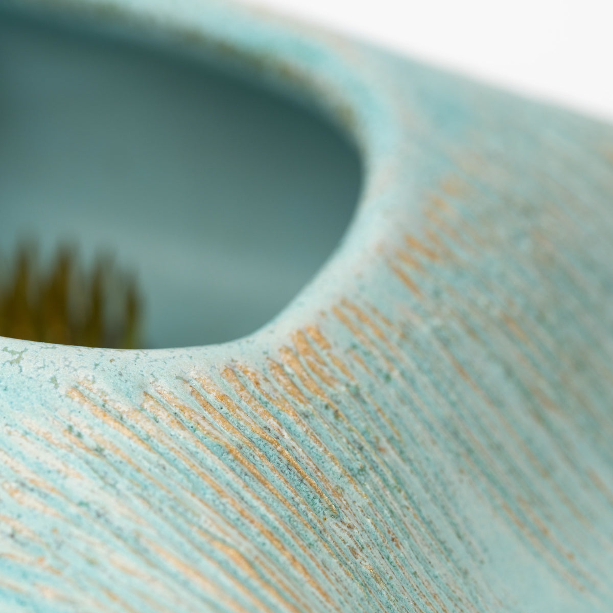 Close-up of combed lines beside the pale blue vase opening.